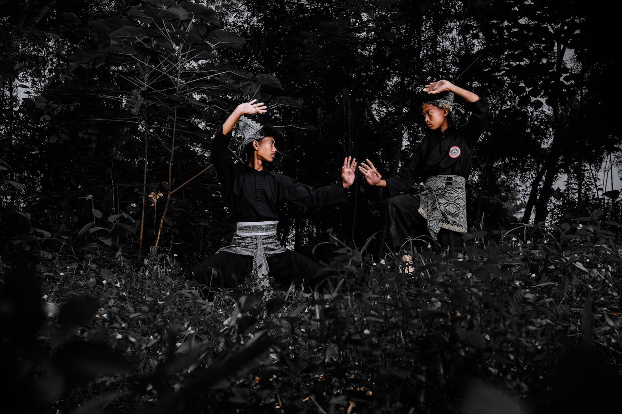 Two individuals practicing Pencak Silat in a dramatic forest setting, emphasizing martial arts form.